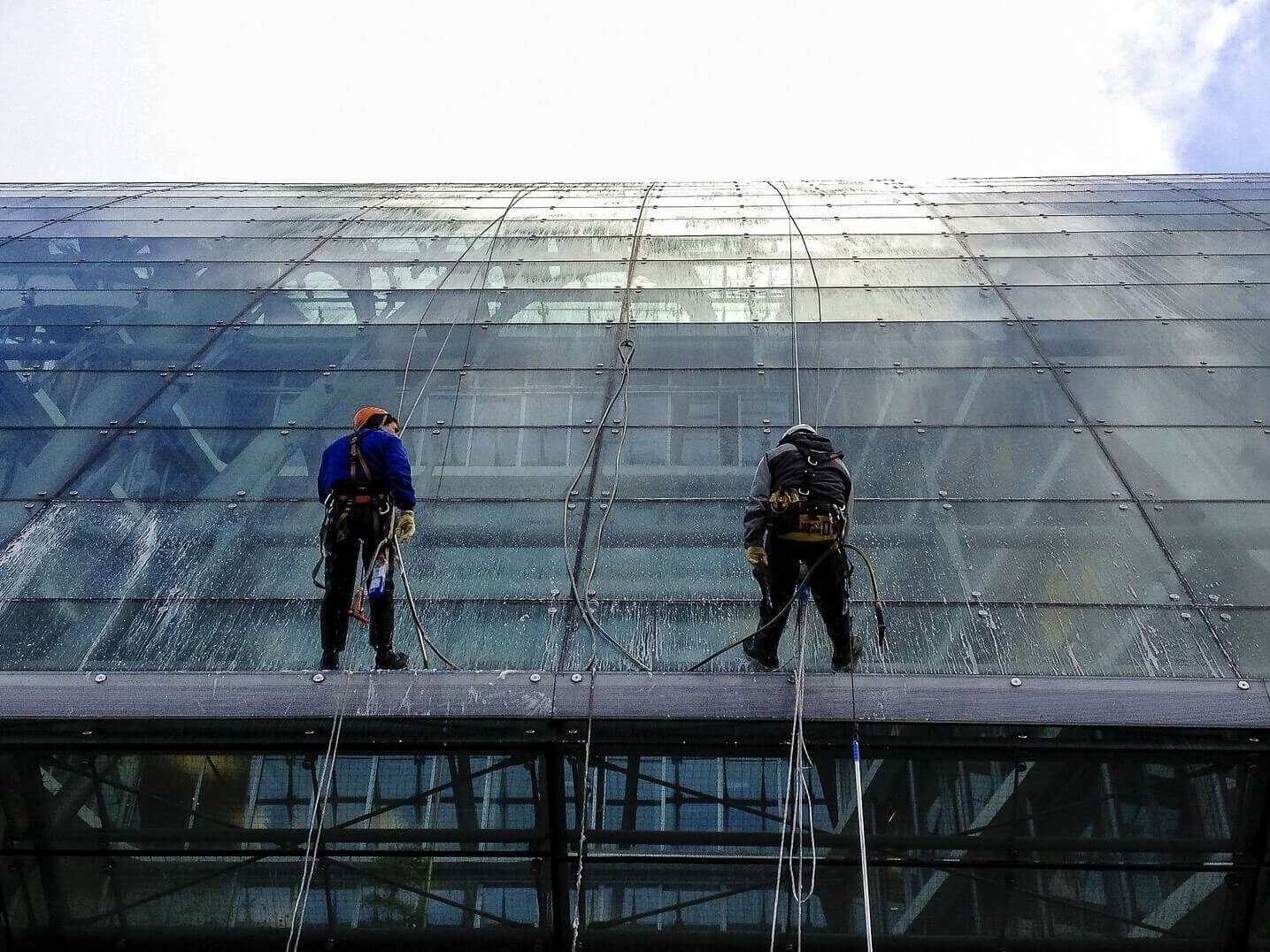 two men wash windows at height using ropes performing window cleaning service at height