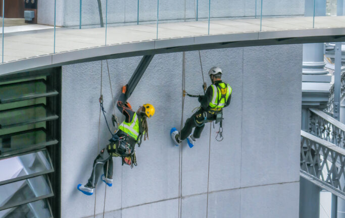 Two workers rappelling down the side of a building