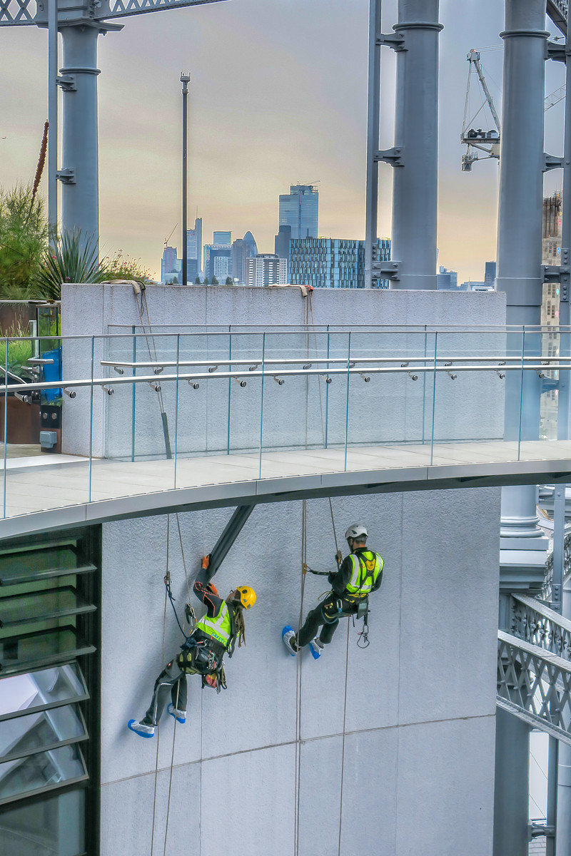 Two workers in safety harnesses suspended by ropes inspecting and repairing the exterior of a tall city building.
