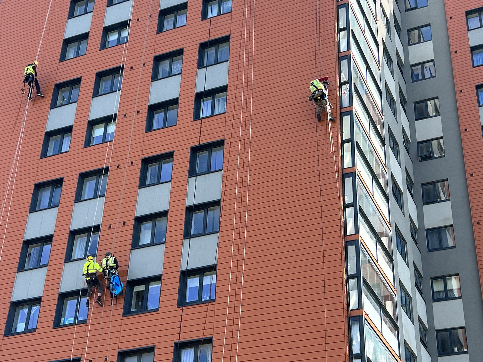 Workers using rope access for exterior maintenance on a tall orange and grey building.
