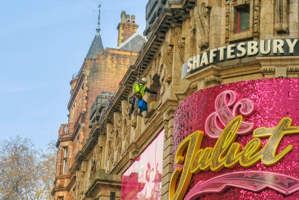 Technician on ropes repairing exterior of Shaftesbury Theatre building.