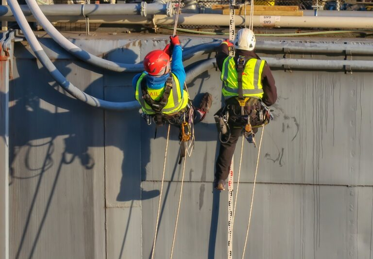 Two workers in safety gear performing high-level inspection on industrial pipes using rope access.