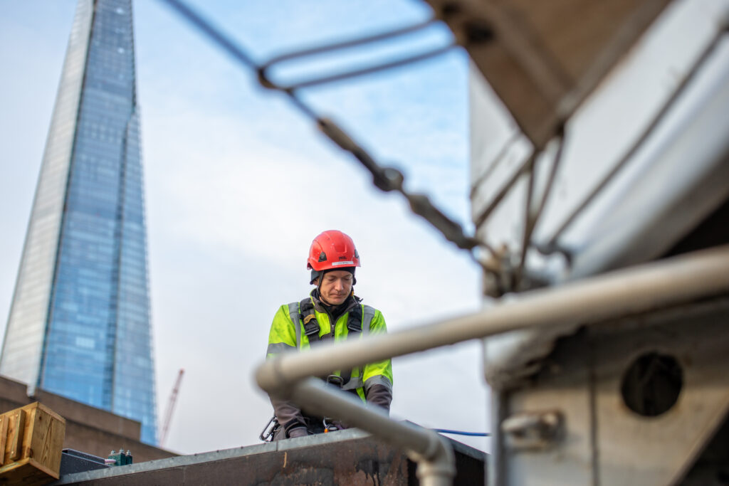Rope access worker in safety gear near The Shard building in London.