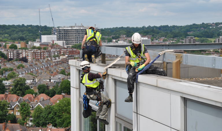 Rope access workers performing tasks on a high-rise rooftop in a city.