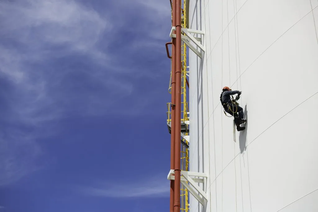 Industrial rope access technician inspecting building facade at height using safety harness