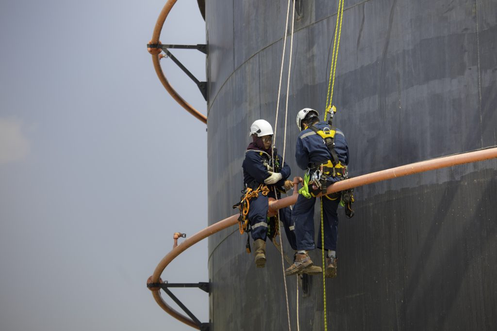 Offshore rope access technicians inspecting industrial storage tank and pipework at height