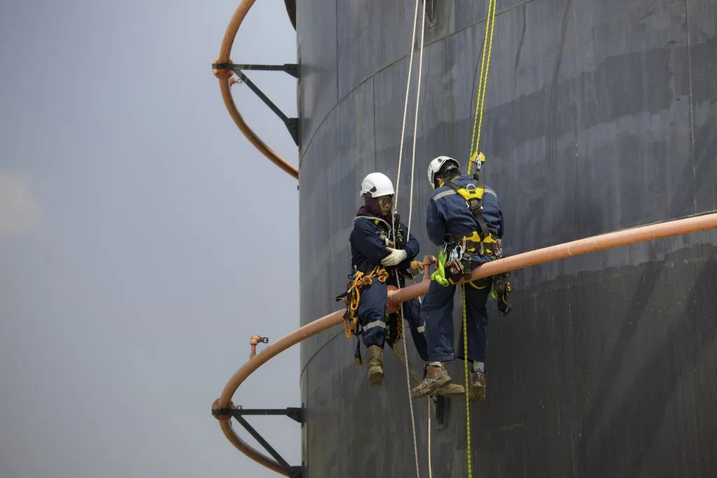 Offshore rope access technicians inspecting industrial storage tank and pipework at height